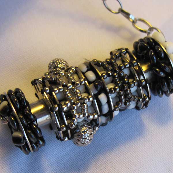 Beaded monochrome pendant of four bobbins in a row woven with beads in square-stitch and brick-stitch patterns