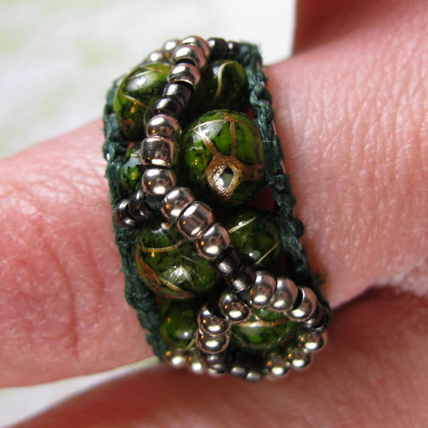 Beaded ring made of a band of an assymetrical netted web of metal seed beads and green-gold round glass beads