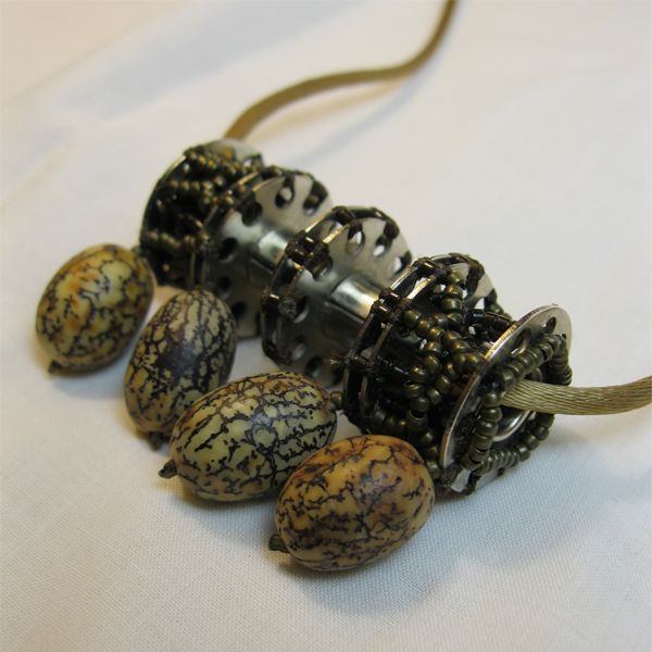 Beaded pendant with a row of assymetrical webbed brown and brass seed beads on bobbins with dangling, elliptical beads made of seeds